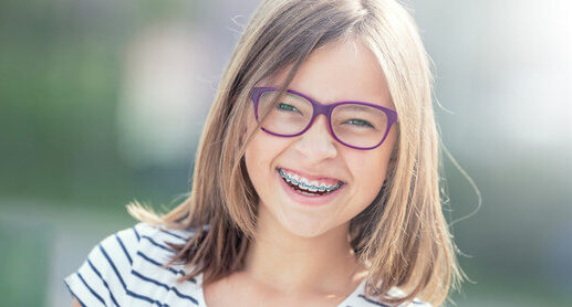 A young girl with glasses smiling with braces on her teeth after an orthodontic appointment