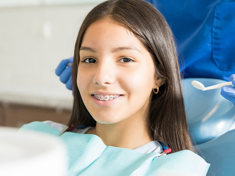 A teenage girl smiling with braces while sitting in a chair in a pediatric office
